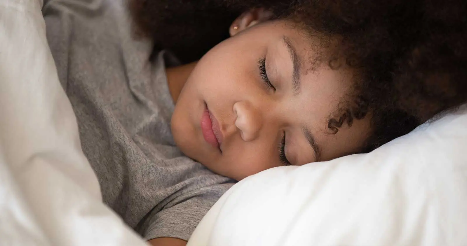Child sleeping in bed with white pillow